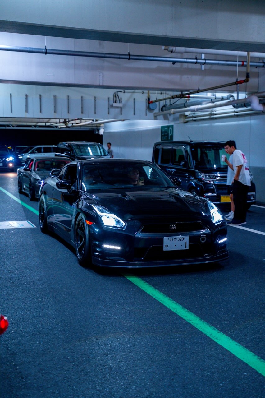 Black Nissan GT-R R35 front with headlights on in a Tokyo parking garage