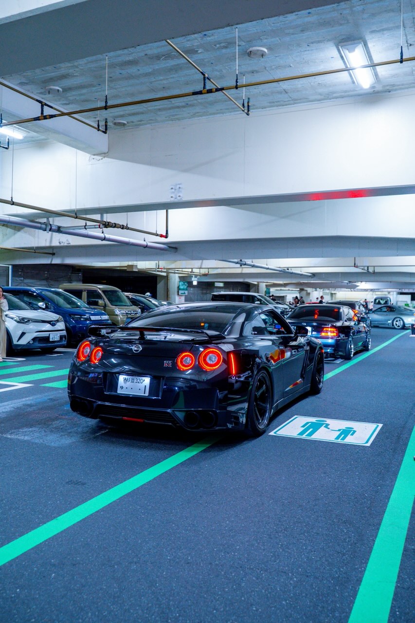 Rear of a black Nissan GT-R R35 with taillights lit in a Tokyo garage at night