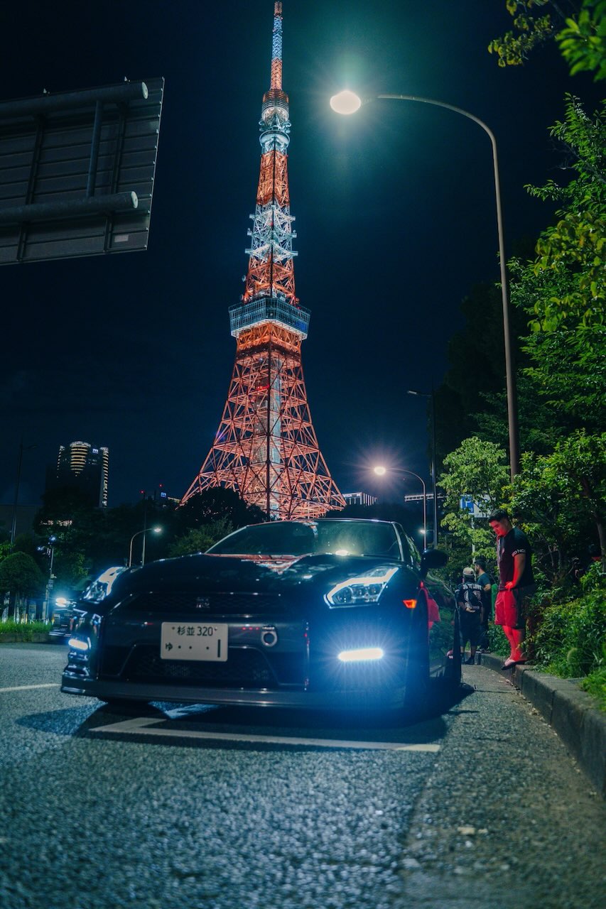 Low angle shot of a Nissan GT-R R35 with Tokyo Tower rising behind it at night