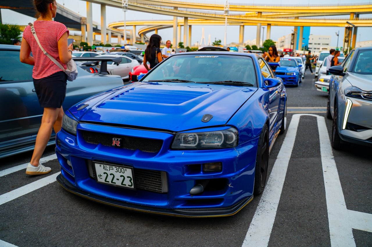 Bayside Blue Nissan Skyline GT-R R34 front three-quarter at Daikoku PA with a second R34 behind
