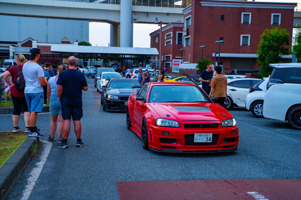 Red Nissan Skyline GT-R R34 with Nismo front bumper at Daikoku PA in the evening