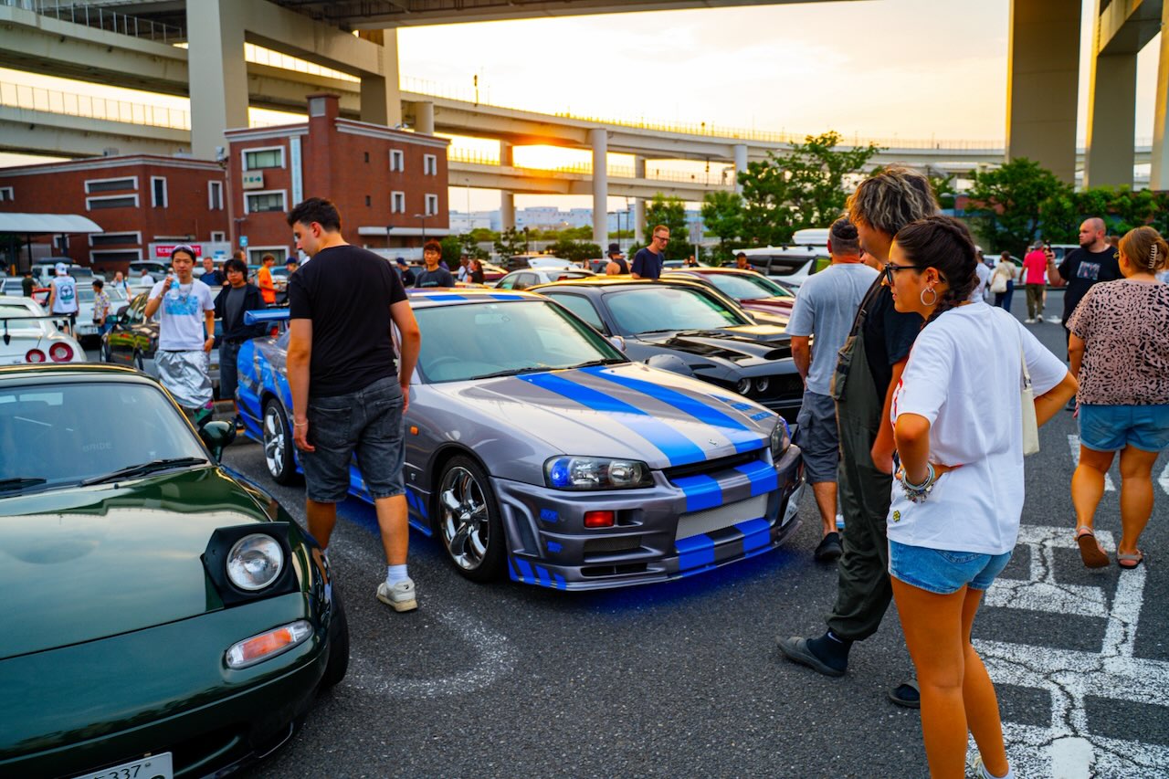 Silver and blue striped Nissan Skyline R34 at Daikoku PA at sunset