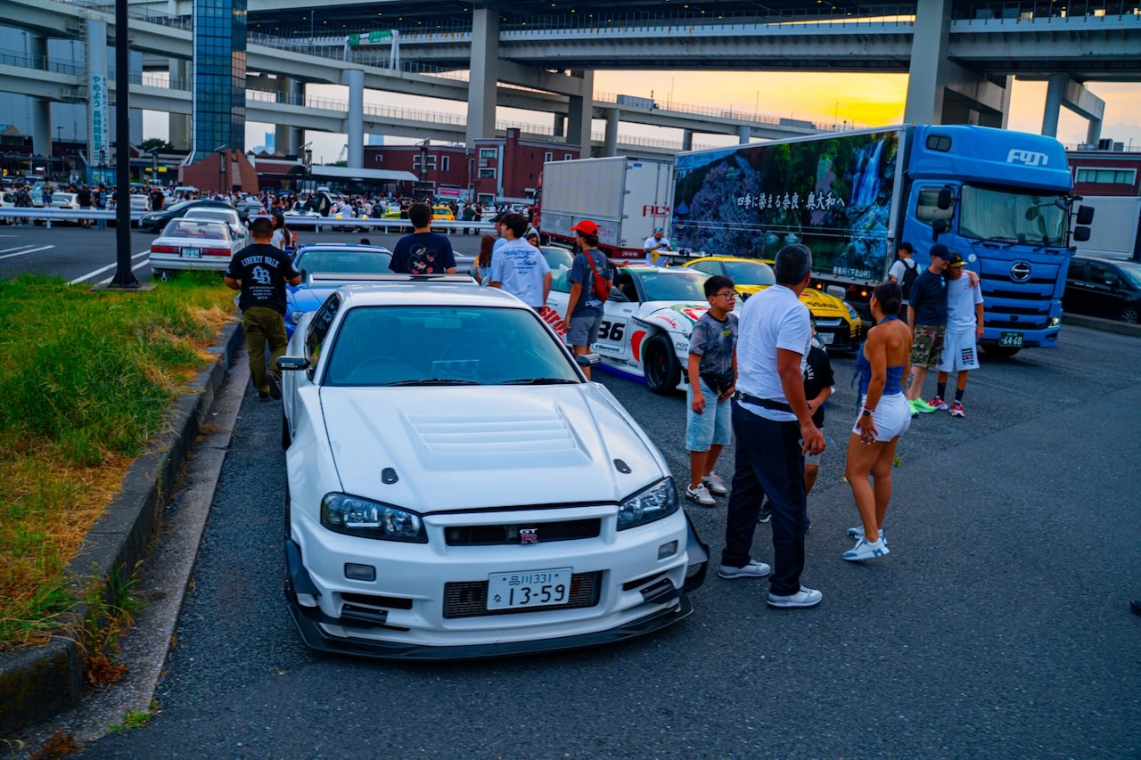 White Nissan Skyline GT-R R34 among other R34s at Daikoku PA at sunset