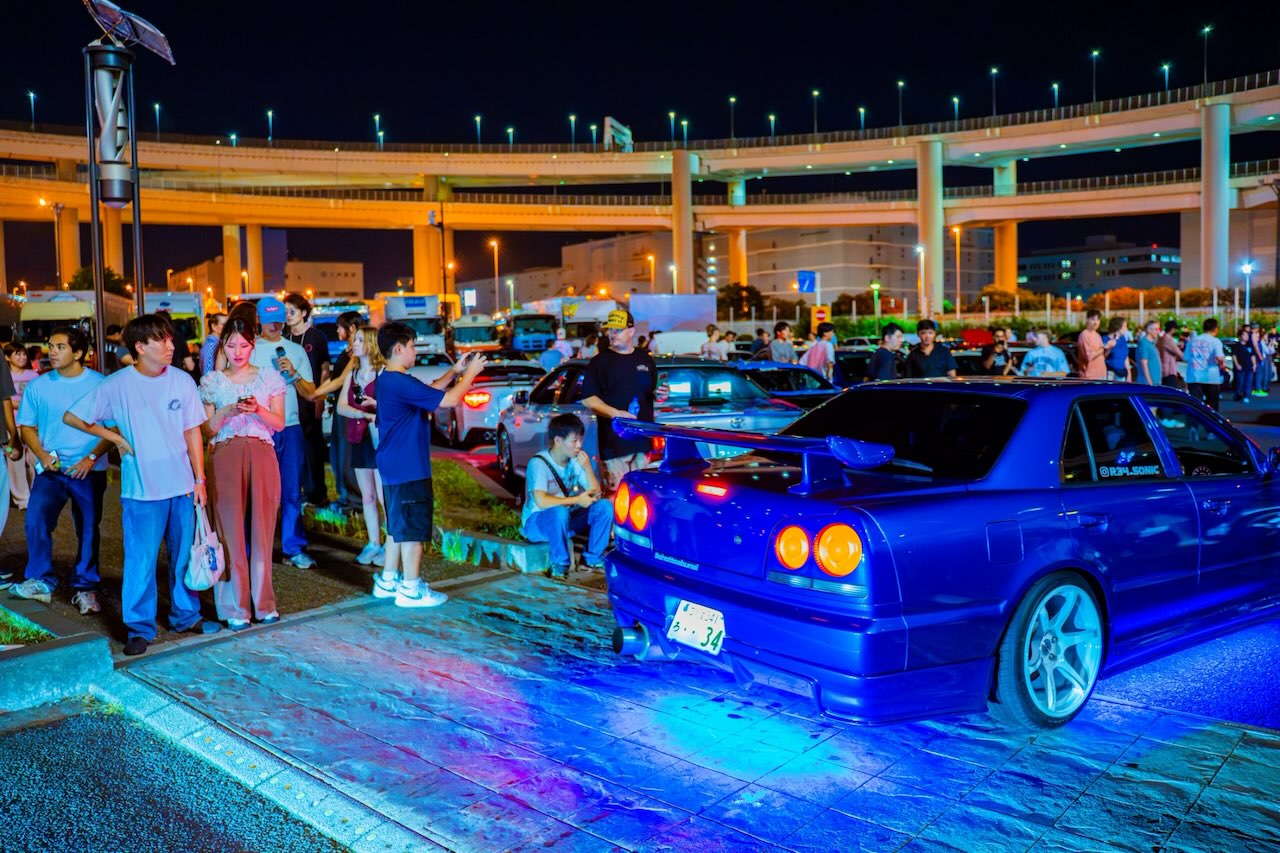 Nissan Skyline rear at Daikoku PA at night with the lit loop ramp behind